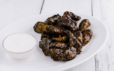 Serving plate presenting stuffed grape leaves dolma with yogurt dip on rustic white table