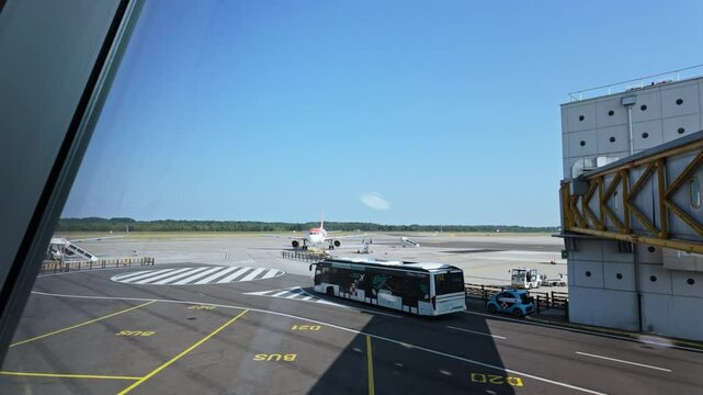 A plane is parked on an empty runway under a clear blue sky at an airport terminal