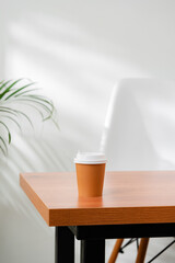 A disposable coffee cup on a wooden table beside a leafy plant