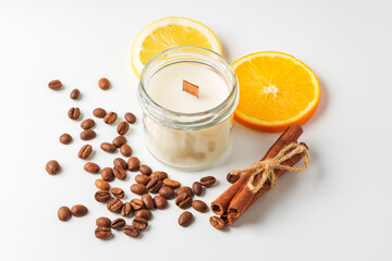 Aromatic candle, coffee beans, orange slices, and cinnamon sticks arranged on a white background