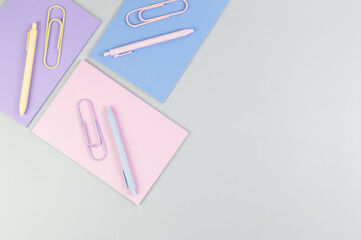 Top view of pink, purple and blue notebooks on grey background. Pink, yellow and blue pens, paperclips, school, office wallpaper. Flat lay, copy space.