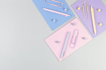 Top view of pink, purple and blue notebooks on grey background. Colorful pens, paperclips, pins, school, office wallpaper. Flat lay, copy space.