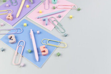 Top view of pink, purple and blue notebooks on grey background. Colorful pens, paperclips, numbers and pins. School, office wallpaper. Flat lay, copy space.