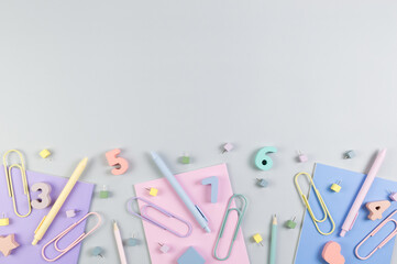 Top view of pink, purple and blue notebooks on grey background. Colorful pens, pencils, paperclips, numbers, shapes and pins. School, office wallpaper. Flat lay, copy space.