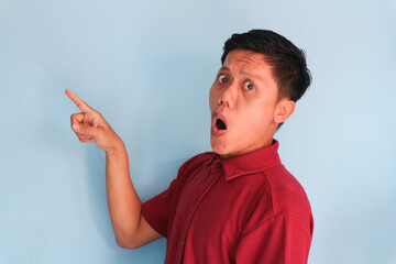 Surprised face of young Asian man in red shirt pointing finger to the side