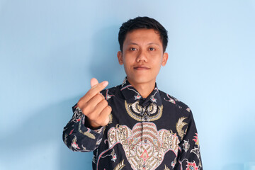 Asian young man wearing batik shirt showing Korean heart love sign