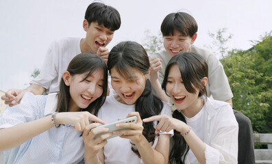  Happy young group of friends using phone and smiling together outdoor.