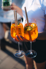Bright and colorful cocktail aperol spritz in a waiter hand in a glove against a background.