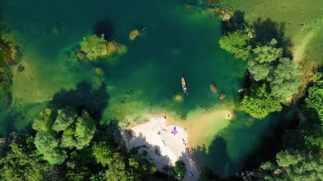 A man with a wooden boat in a beautiful clear river with people on the beach and swimming - top view - drone footage - Una River in Bosnia and Herzegovina