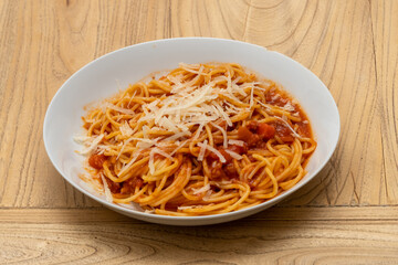 a plate of spaguettis with tomato and meat sauce, bolognese sauce, with grated cheese on top on a white plate on a wooden table