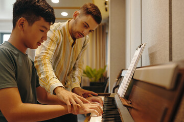 Young Asian boy learning piano while an instructor guides his hands in a well-lit modern room creating an engaging educational experience
