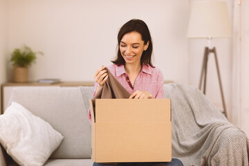 Happy young female volunteer sorting clothing donations in cardboard box, copyspace