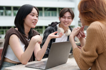 Attractive Asian college students using laptop, tablet, mobile phone to study online social media Finding knowledge together, talking, working as a team. Educational concept success in life.