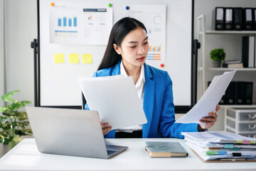 A woman in a blue jacket is reading papers at her desk