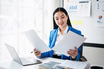 A woman in a blue jacket is sitting at a desk with a laptop