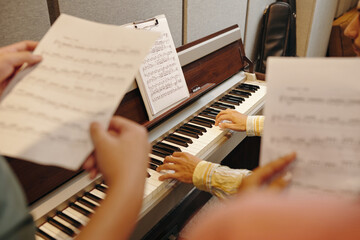 Musicians' hands playing piano with sheet music stand in foreground creating a musical atmosphere...