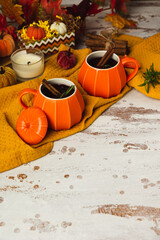 Two pumpkin cups of autumn mulled wine with cinnamon on rustic table. Traditional fall spiced drink in orange ceramic mugs. Decorative textile pumpkins and candles