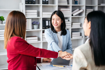 Fototapeta premium Three women in business attire shake hands in a conference room