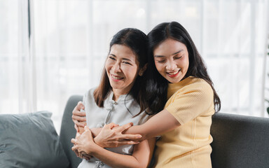 Cheerful spending time together of asian daughter hugging her mother laughing embracing happy senior aged mom having fun at living room home