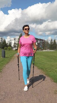 Athletic active mature woman in sportswear doing Nordic walking in a city park in Finland