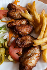 Close up of chicken wings with fries and salad.