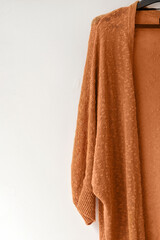 Cozy autumn knitted cardigan hanging on hanger, on white empty background, fashion seasonal clothing concept