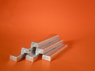 A stack of silver metal bars on a red background. The bars are stacked in a pyramid shape. Invest in precious metals to keep value of money against rising inflation concept.