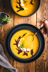 Eine Frau hält einen Löffel in eine frische Kürbissuppe auf einem braunen Holztisch. Draufsicht,...