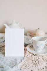 Mockup card,  teacup and saucer are on a table with a plate, tea time