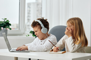 Smiling boy and girl studying together at home on their laptops, fully absorbed in their online elearning activities They sit at a table in the cozy living room, wearing headphones, completely engaged