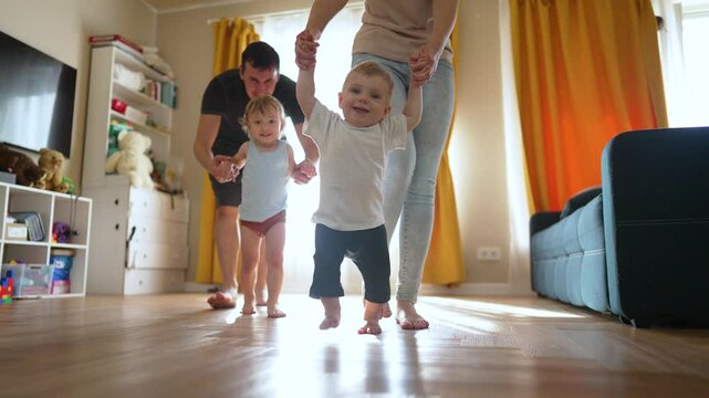 Toddler takes first steps with mother and father. Family helps toddler learn to walk. Toddler milestone of first steps. Proud mother and father assist toddler. Joyful family moment as steps forward.