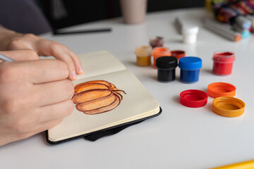 Finalizing a pumpkin painting with gouache in a sketchbook