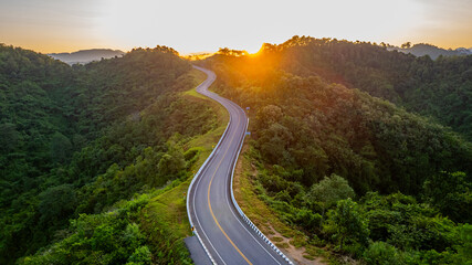 A mountain road with many curves winding through lush and lush forests and beautiful natural views on both sides during the morning sunrise in Nan Province, Thailand, Asia.