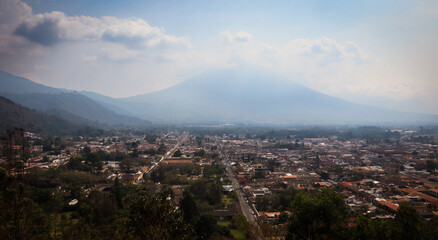 Aerial view of Antigua, Guatemala showcasing the vibrant city nestled beneath majestic volcanic mountains in the afternoon light