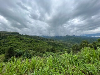 Obraz premium Vast mountainous landscape under a dramatic cloudy sky, with lush green hills and dense vegetation. A breathtaking view of nature, perfect for travel and outdoor adventure themes.