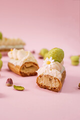 French sweet dessert Eclair cake cut in half with white creme and pistachio macarons on pink background