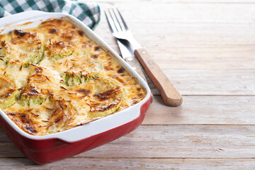 Casserole with cheese and gratin zucchini on wooden table. Copy space