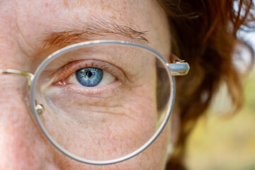 Detailed closeup of the left  blue gray eye of a serious middle aged red haired woman wearing...