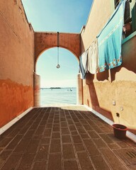 A view of the Cannaregio district in Venice, with an arched passage leading to a serene waterfront. Laundry hangs drying in the sunlight, adding a charming touch to this hidden spot.