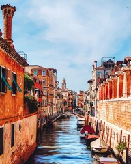 Venetian canal view featuring Ponte de Ca' Bala with gondolas, bordered by colorful historic buildings and the Leaning Santo Stefano Tower, a prominent medieval structure in the city.