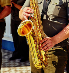 Golden saxophone held by a musician during a vibrant street performance in a sunlit urban setting...