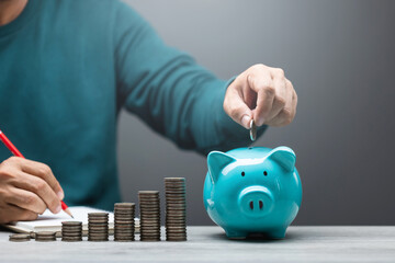 Man is dropping coins into a blue piggy bank, symbolizing the act of saving and financial responsibility. Financial planning, budgeting, and building a stable future through consistent savings