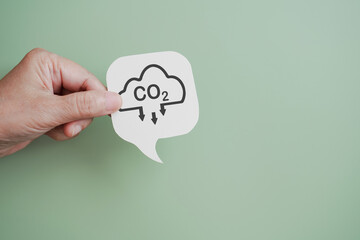 hand hold real white speech bubble with co2 text inside cloud and down arrow on green background including copy space