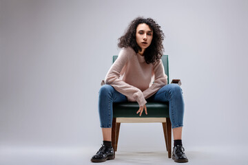 Fashion model posing sitting on vintage armchair with legs sprea