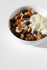 Breakfast Food. Bowl with Cottage Cheese Served with Granola, Nuts, Seeds and Blueberries on White Background. 