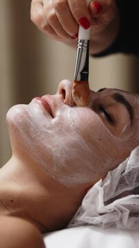 Close-up of a cosmetologist applying a mask to a client's face in a spa salon. This scene highlights the attentive application of skincare treatments in a serene and professional environment.