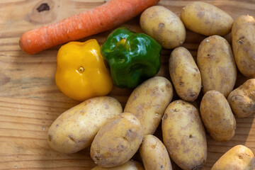 Potatoes, green, yellow bell peppers, carrot on a rustic wooden cutting board for healthy cooking and meal preparation. A vibrant assortment of fresh vegetables farm-to-table concept. Top view