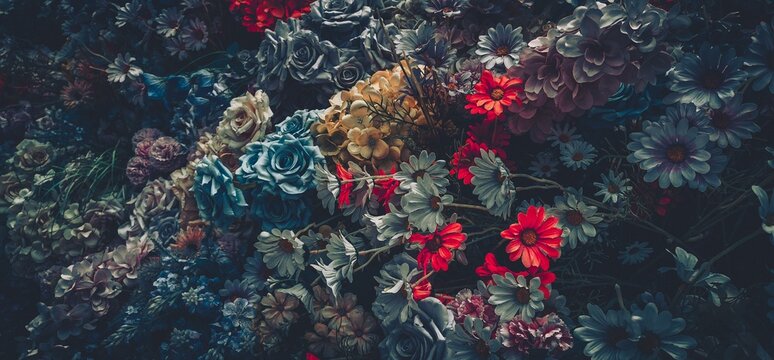 A close-up of a vintage bouquet of artificial flowers in shades of blue, red, and white, with dark green foliage.