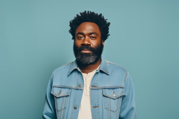 Fototapeta premium Portrait of a content afro-american man in his 40s sporting a rugged denim jacket in front of pastel teal background