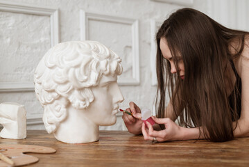 Female artist applying red tint on plaster head model lips